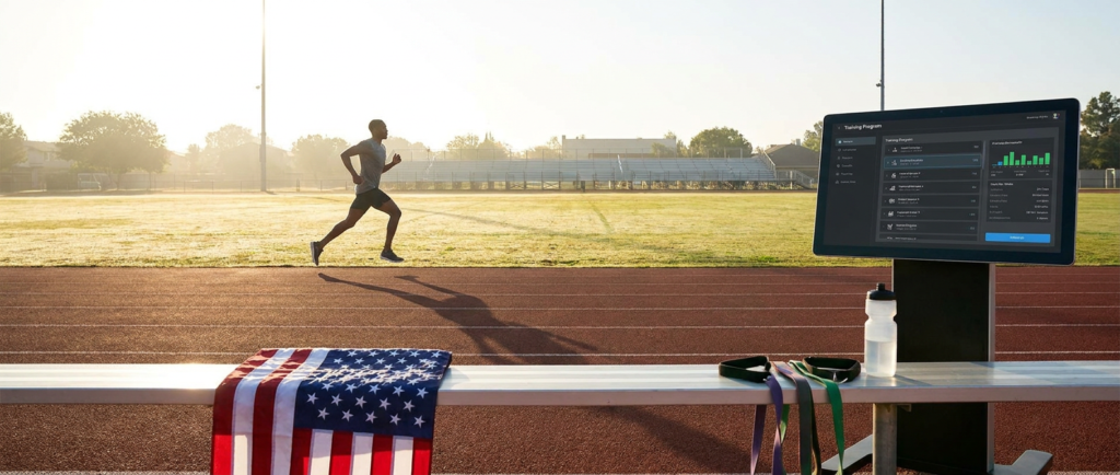 athlete running on a track near a screen displaying memorial day training schedules, with an american flag.