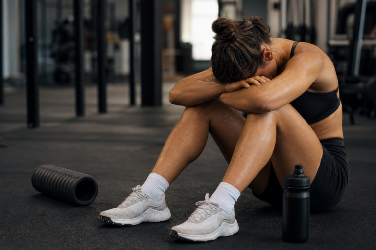 sweaty female athlete resting on the gym floor with a foam roller, depicting athletic recovery techniques.